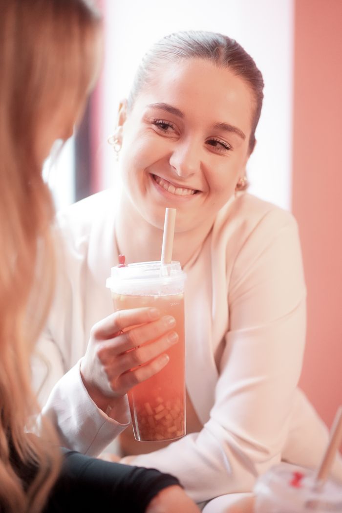 Woman smiling while holding a cup of bubble tea inside a bright café.