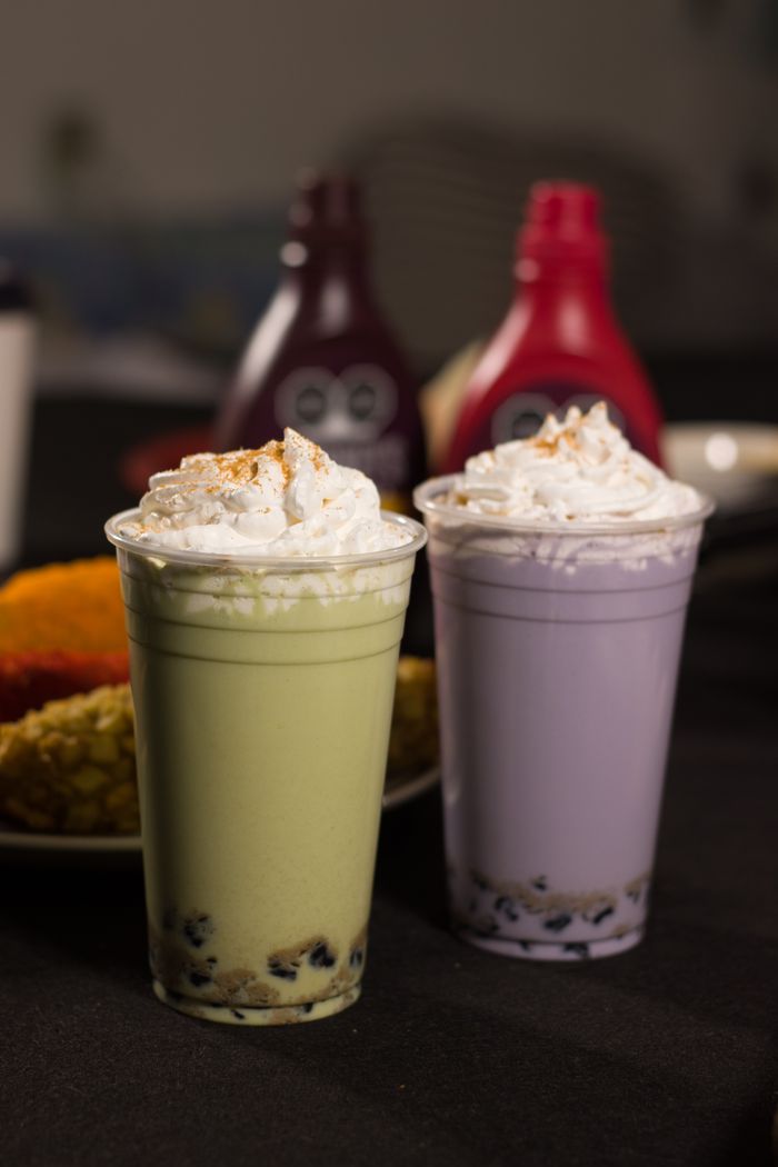 Two colorful boba milk teas with whipped cream, featuring vibrant green and purple colors.