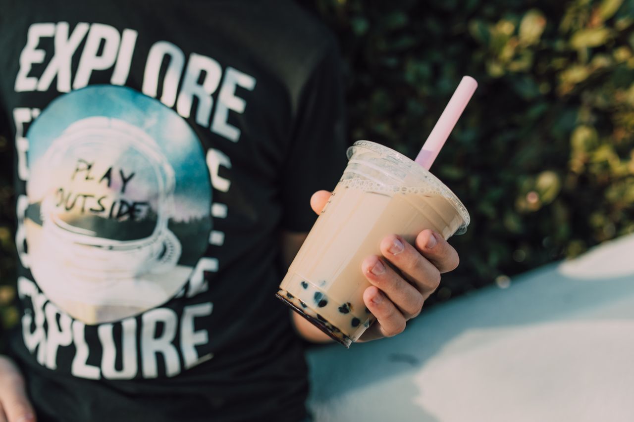 Close-up of a person holding delicious bubble tea outdoors, with vibrant surroundings.